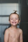 Portrait of cheerful little boy standing in shower with wet hair — Stock Photo