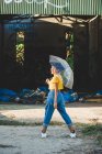 Молода жінка в стильному вбранні позує з прозорою парасолькою на вулиці в сонячний день — стокове фото