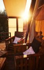 Chaises en bois marron avec oreiller coloré sur sol en bois avec tente beige et feuillage vert avec rayons de soleil sur le fond — Photo de stock