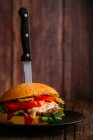 Deliciosa hamburguesa gourmet con cuchillo en plato sobre fondo de madera oscura - foto de stock