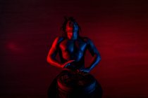 Giovane uomo rastafariano africano gode di prove e gioca tam tam, illuminazione colorata rosso e blu — Foto stock