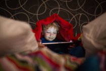 Petit garçon souriant en pyjama utilisant une tablette numérique sous la couverture — Photo de stock