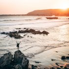 Vue arrière de la femme touristique debout les mains écartées sur la pierre côtière et se sentant libre au bord de la mer. — Photo de stock