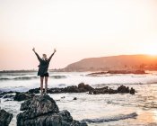 Rückansicht einer Touristin, die mit den Händen auseinander auf einem Küstenstein steht und sich am Meer frei fühlt. — Stockfoto