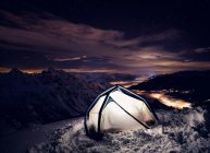 Tenda com luz acesa nas montanhas cobertas de neve à noite. — Fotografia de Stock
