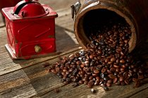 Zusammensetzung von Metall schäbigen Vintage-Mühle und verschütteten Haufen aromatischer Kaffeebohnen auf Holztisch — Stockfoto