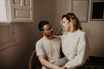 Happy couple sitting in armchair and looking at each other while bonding at home — Stock Photo