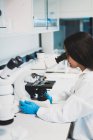 Brunette femme en uniforme en utilisant le microscope en laboratoire — Photo de stock