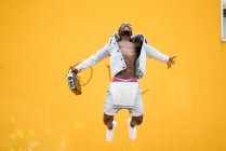 Афроамериканський чоловік стрибає з вінтажним радіопристроєм на жовтому фоні — стокове фото