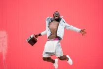 Uomo africano americano che salta con dispositivo radio vintage su sfondo rosso — Foto stock