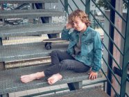 Pieds nus garçon assis sur les escaliers avec planche à roulettes — Photo de stock
