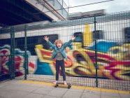Смішний босоніж хлопчик на скейтборді з піднятими руками перед поїздом — стокове фото