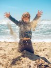 Kleiner Junge spielt und wirft Sand auf dem Hintergrund des Ozeans in sonnigem Tag — Stockfoto