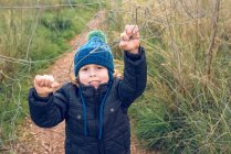 Niño pequeño de pie y sosteniendo cerca de alambre en el campo - foto de stock