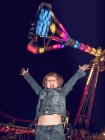 Petit garçon émotionnel debout les mains en l'air sur le fond du carrousel la nuit — Photo de stock