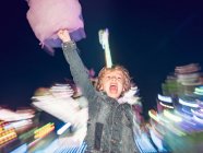 Petit garçon excité debout avec de la soie dentaire rose bonbons sur fond de fête foraine floue la nuit — Photo de stock