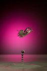 Крупный план брызг прозрачной жидкости цвета на розовом фоне — стоковое фото