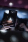 Крупным планом женской руки с помощью смартфона в размытой темной комнате — стоковое фото