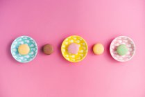 De cima brilhantes deliciosos macarons em placas no fundo rosa — Fotografia de Stock