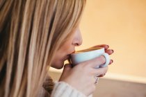 Side view crop attractive woman in sweater holding mug ofhot drink near lips — Stock Photo