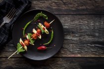 Macarrones con tomate y albahaca en palo sobre plato negro con salsa sobre madera oscura - foto de stock