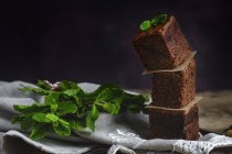 Stacked pieces of chocolate brownie with mint on dark background — Stock Photo