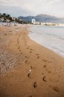 Huellas de pies humanos sobre arena mojada cerca del mar ondulante en Altea, España - foto de stock