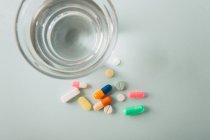 Comprimidos multicoloridos e cápsulas com vidro de água sobre fundo branco — Fotografia de Stock