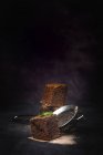 Pieces of chocolate brownie with mint on dark background with strainer — Stock Photo