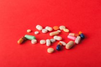 Різнокольорові таблетки та капсули, розкидані на червоному тлі — стокове фото