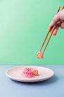 From above person hand with chopsticks holding slice of tasty donut on dish on blue background — Stock Photo