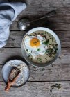 Миска смачної зернової каші зі смаженим яйцем на дерев'яній тарілці — стокове фото