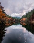 Ruhiger Fluss zwischen Herbstwald und Hügeln unter bewölktem Himmel — Stockfoto