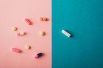 Таблетки и капсулы, разбросанные на голубом и розовом фоне — стоковое фото