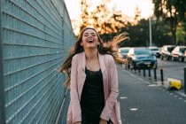 Laughing young woman walking on street near cars at sunset — Stock Photo