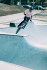 Jovem de camiseta branca e capacete montando BMX no trampolim no fundo da estrada e carros — Fotografia de Stock