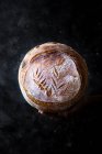 Closeup of human hand holding loaf of fresh bread on dark background — Stock Photo