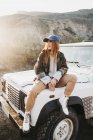 Attractive red haired woman looking away and sitting on off-roader near hills — Stock Photo