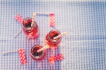Bottles with fresh fruit drink and drinking straws on checkered tablecloth — Stock Photo