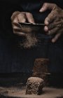 Человеческие руки порошок кусочки шоколадного брауни с какао на темном фоне — стоковое фото