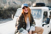 Junge Frau in Freizeitkleidung blickt in die Kamera und sitzt auf dem Auto — Stockfoto