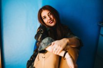 Lächelnde attraktive Frau sitzt neben blauer Wand — Stockfoto
