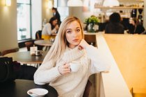 Joven mujer encantadora sosteniendo taza en la cafetería - foto de stock