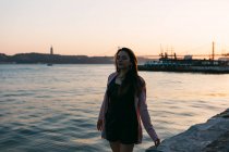 Dreamy young girl walking on embankment near water surface at sunset — Stock Photo