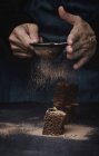 Человеческие руки порошок кусочки шоколадного брауни с какао на темном фоне — стоковое фото