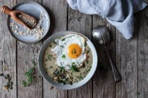 Ciotola di porridge di grano buonissimo con uovo fritto su tavoletta di legno — Foto stock