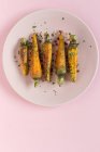 Gesunde geröstete Karotten mit Kräutern und Gewürzen auf Teller auf rosa Hintergrund — Stockfoto
