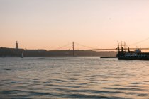 Pittoresco ponte vista sopra l'acqua ondulata con barche galleggianti e cielo rosa al tramonto — Foto stock