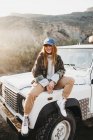 Junge Frau in Freizeitkleidung sitzt auf Auto — Stockfoto