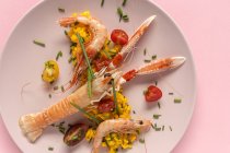 Paella casera con cangrejos de río y gambas en plato sobre fondo rosa - foto de stock